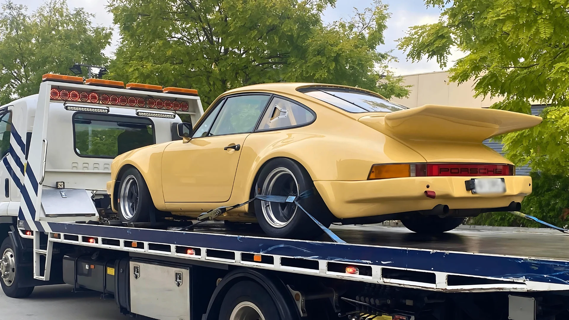 A yellow Porsche 911 strapped down on the All Over Towing tilt tray