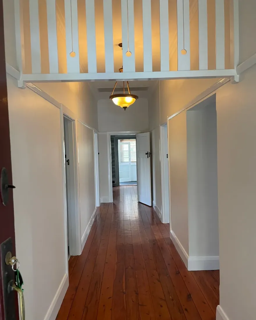 A Murrays Painting Facebook post: the hallway of an older home after a repaint, with white walls and trim over timber floorboards.