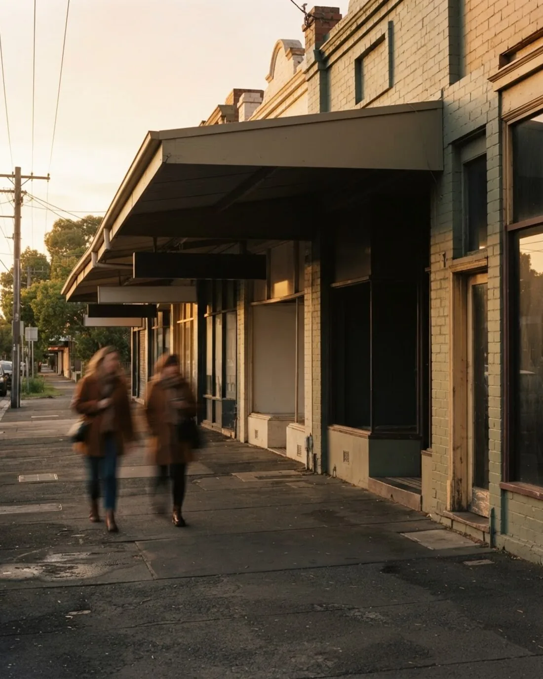 A suburban high street shopfront strip at golden hour with passers-by blurred
