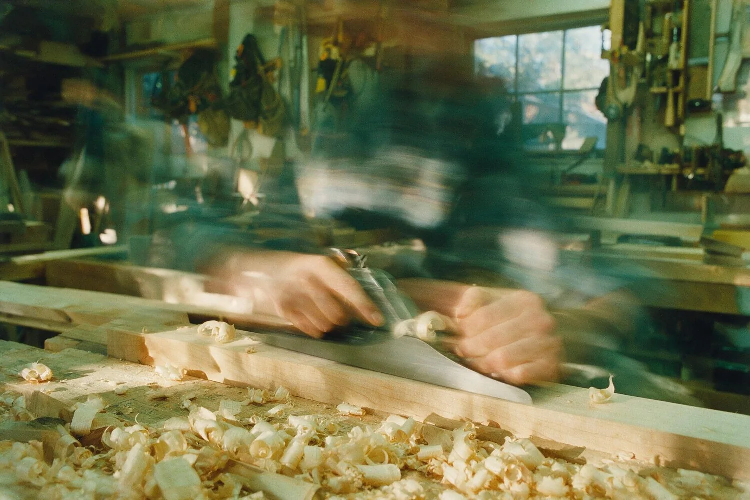 Hands working timber at a bench, the workshop blurred around them
